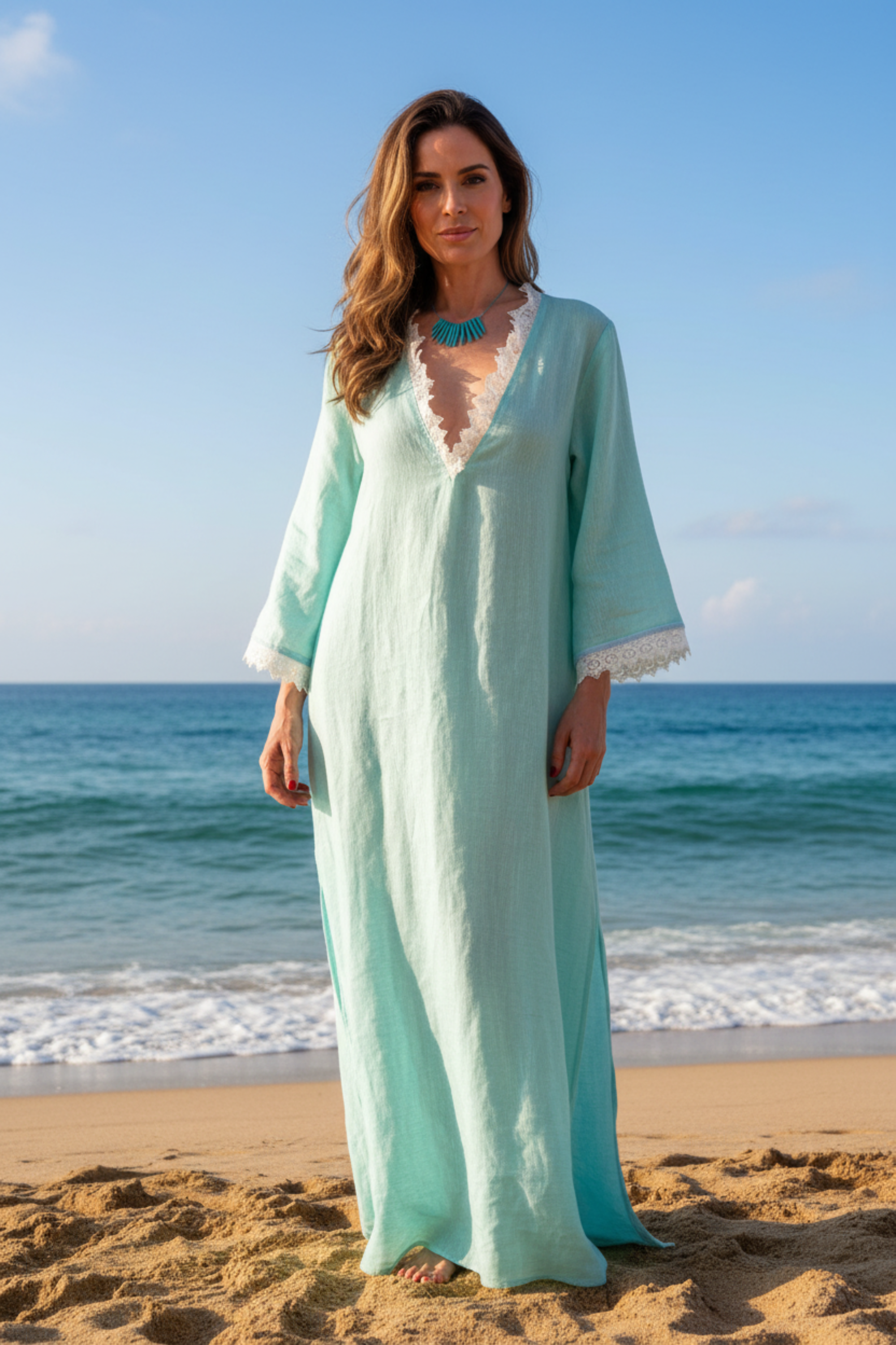 Woman in a light blue dress standing on a beach with ocean waves in the background